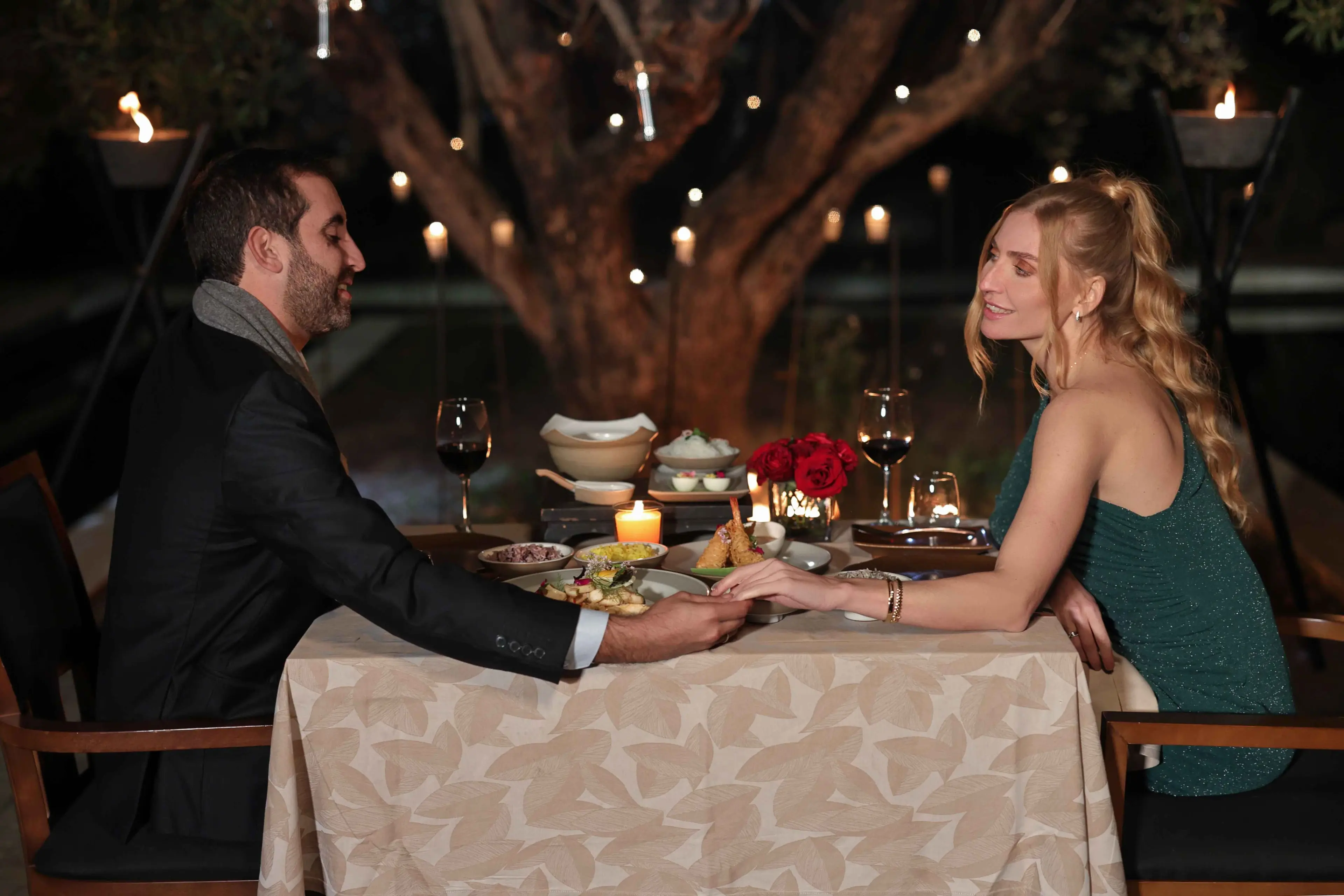 Couple dining romantically under tree lights at Banyan Tree Tamouda Bay, holding hands across table.